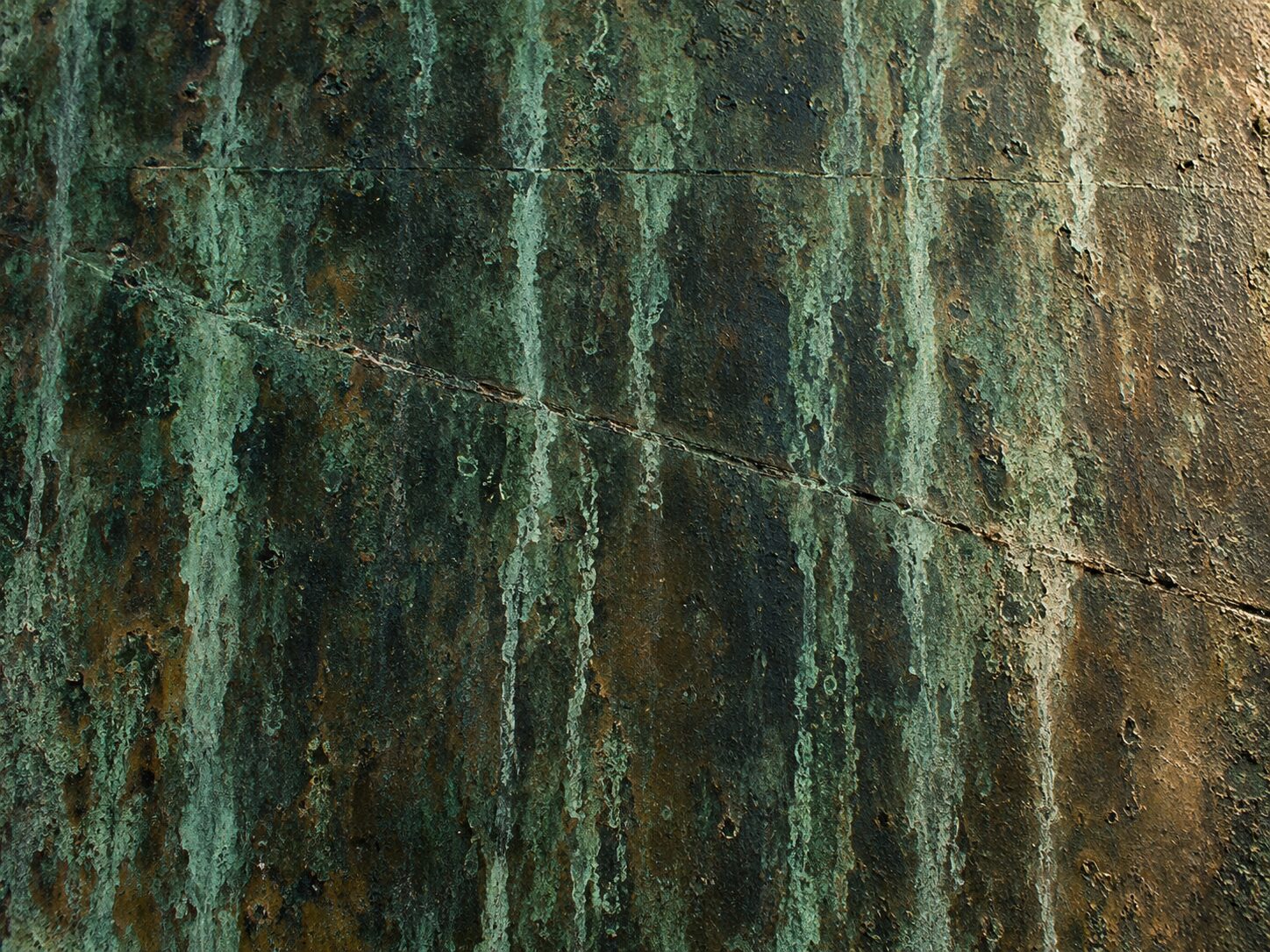 A flat bronze plate weathered to green-black patina, crossed by vertical verdigris run-off streaks and one shallow diagonal crease.