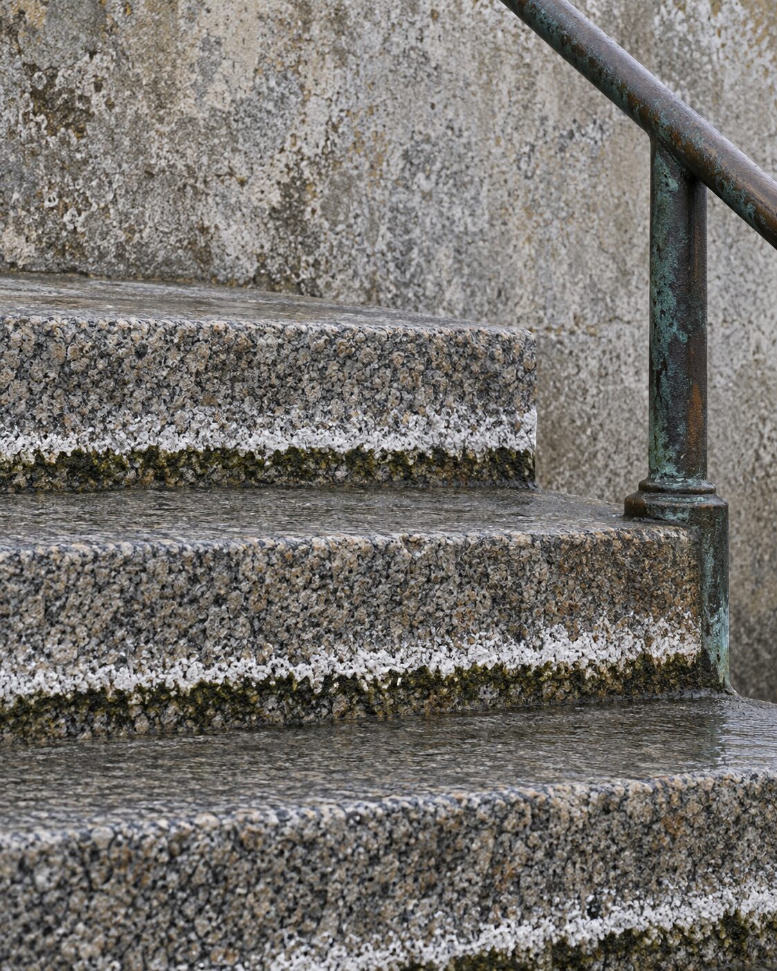 Worn granite steps with a bronze handrail, a tide line of salt bloom and dark moss crossing the treads at one height.
